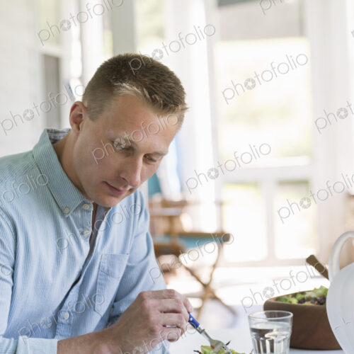 A man seated at a cafe table eating a salad and reading a book. A man seated at a cafe table eating a salad and reading a book.