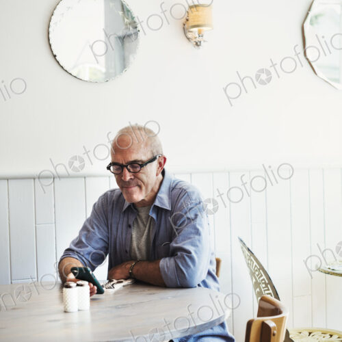 A man seated at a table checking his smart phone. A man seated at a table checking his smart phone.
