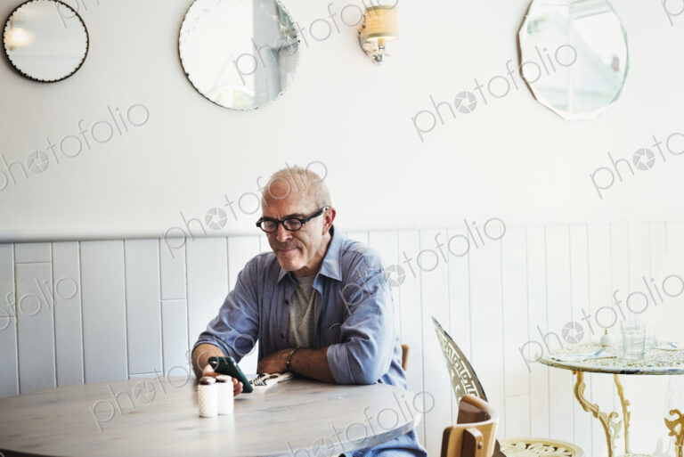 A man seated at a table checking his smart phone.