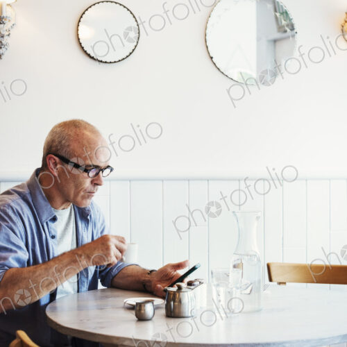 A man seated at a table checking his smart phone. A man seated at a table checking his smart phone.