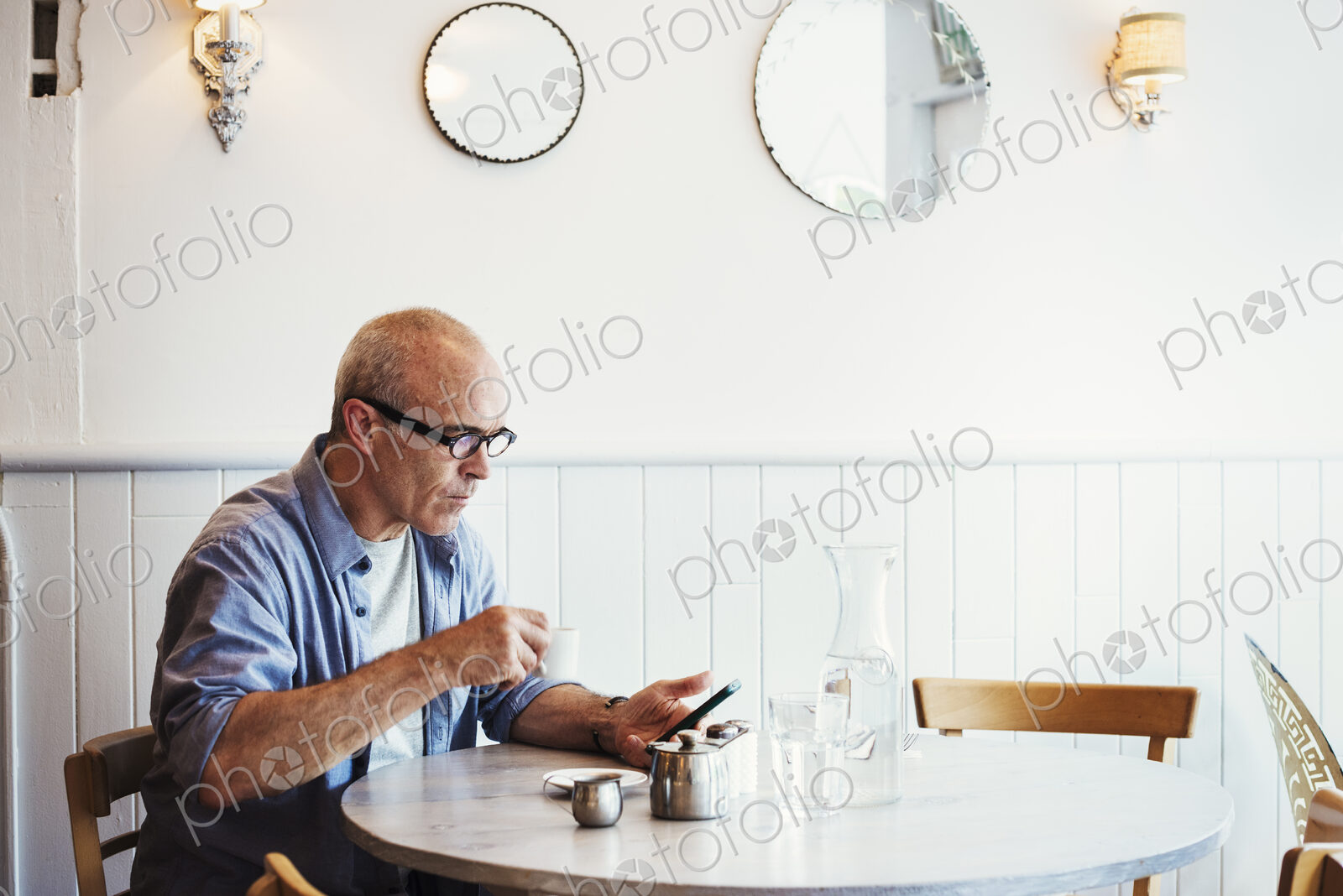 A man seated at a table checking his smart phone.