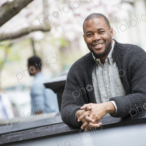 A man seated at a table outdoors, two people in the background. A man seated at a table outdoors, two people in the background.