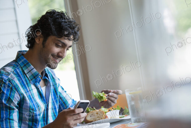 A man seated checking his phone, and eating in a cafe.
