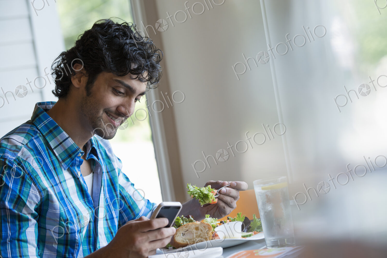 A man seated checking his phone, and eating in a cafe.