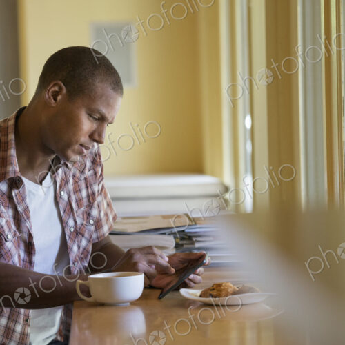 A man seated having a cup of coffee, holding a digital tablet. A man seated having a cup of coffee, holding a digital tablet.