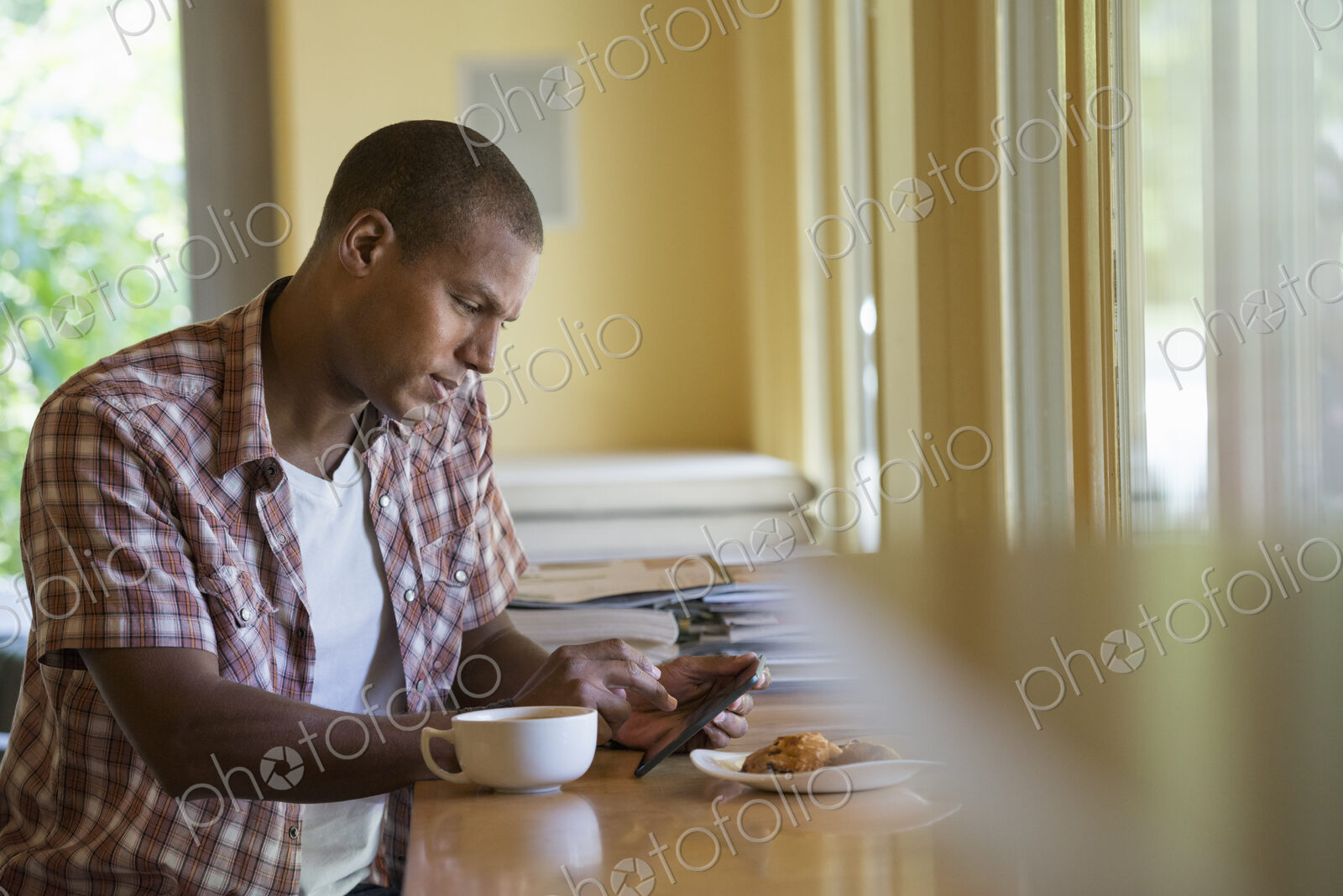 A man seated having a cup of coffee, holding a digital tablet.