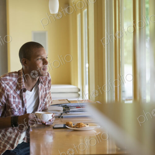 A man seated having a cup of coffee, holding a digital tablet. A man seated having a cup of coffee, holding a digital tablet.