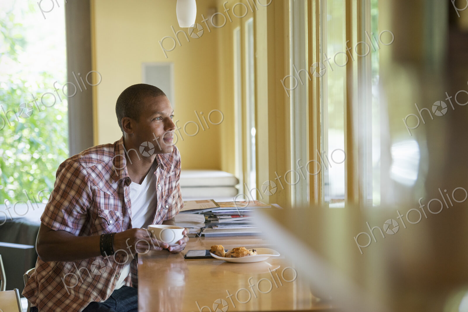 A man seated having a cup of coffee, holding a digital tablet.