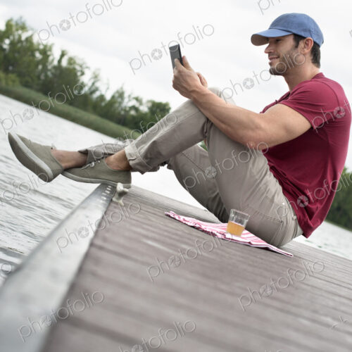 A man seated on a jetty by a lake, using a digital tablet. A man seated on a jetty by a lake, using a digital tablet.