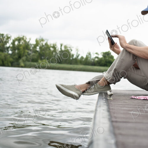 A man seated on a jetty by a lake, using a digital tablet. A man seated on a jetty by a lake, using a digital tablet.
