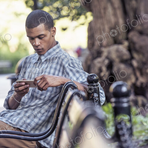 A man seated on a park bench using his smart phone A man seated on a park bench using his smart phone