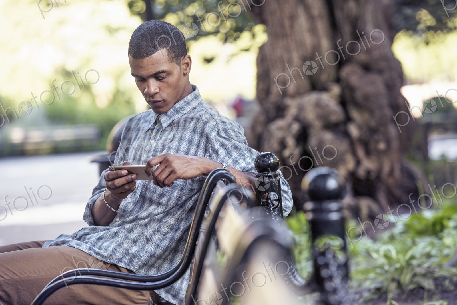 A man seated on a park bench using his smart phone