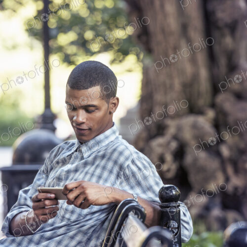 A man seated on a park bench using his smart phone A man seated on a park bench using his smart phone