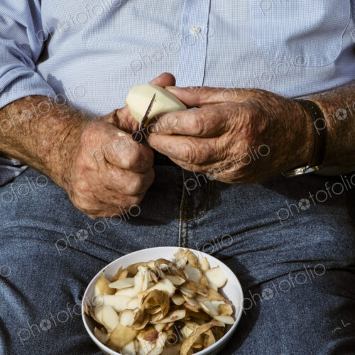 A man seated using a sharp knife to peel potatoes.