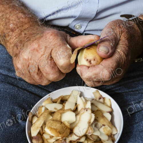 A man seated using a sharp knife to peel potatoes.