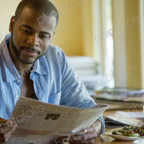 A man sitting along in a cafe, reading a newspaper. A man sitting along in a cafe, reading a newspaper.