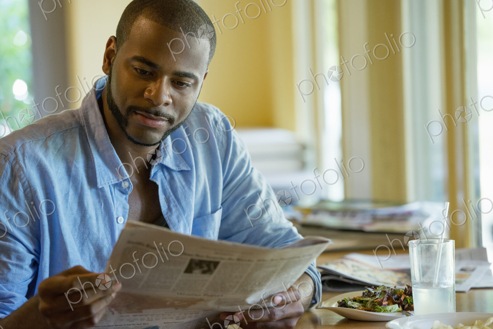 A man sitting along in a cafe, reading a newspaper.