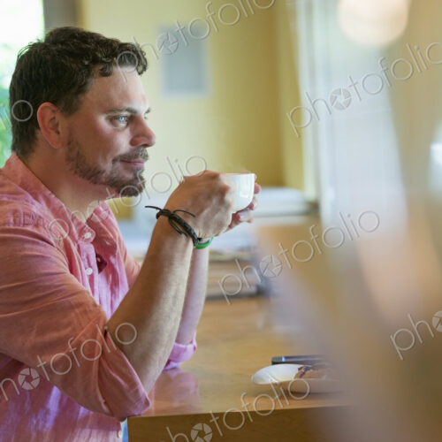 A man sitting at a cafe table, holding a cup of coffee.