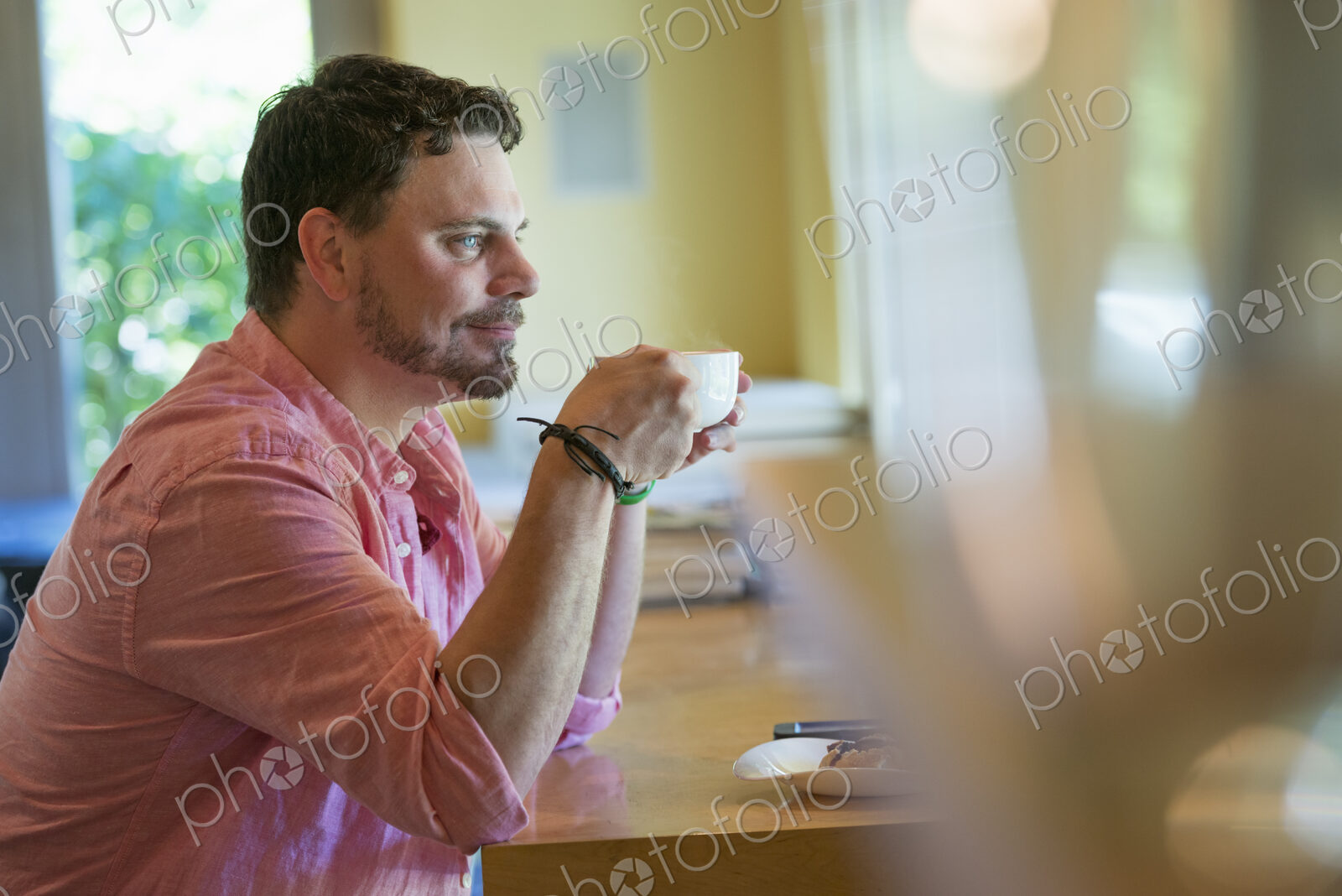 A man sitting at a cafe table, holding a cup of coffee.