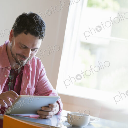 A man sitting at a cafe table, using a digital tablet. A man sitting at a cafe table, using a digital tablet.