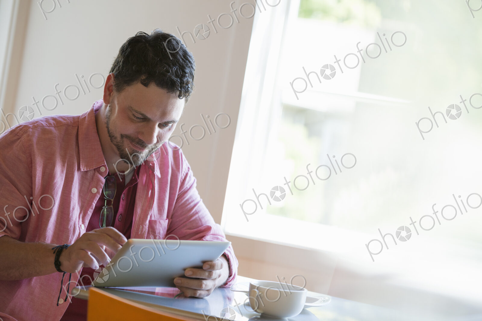 A man sitting at a cafe table, using a digital tablet.