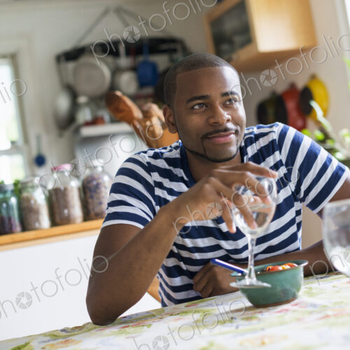 A man sitting at a table eating dessert, holding a glass of wine.