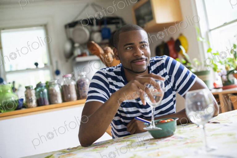 A man sitting at a table eating dessert, holding a glass of wine.