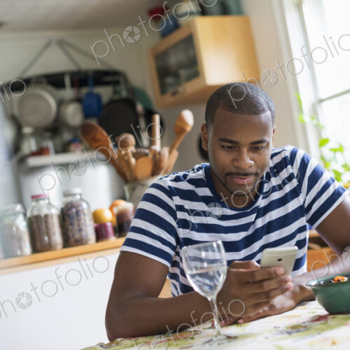 A man sitting at a table using a smart phone. Fruit dessert and a glass of wine at hand.