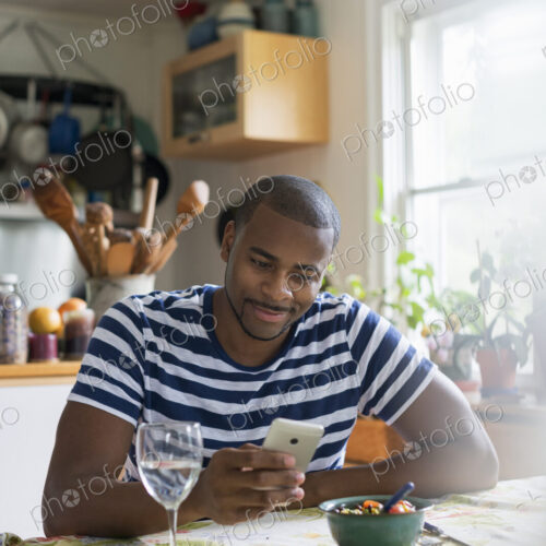 A man sitting at a table using a smart phone. Fruit dessert and a glass of wine at hand.