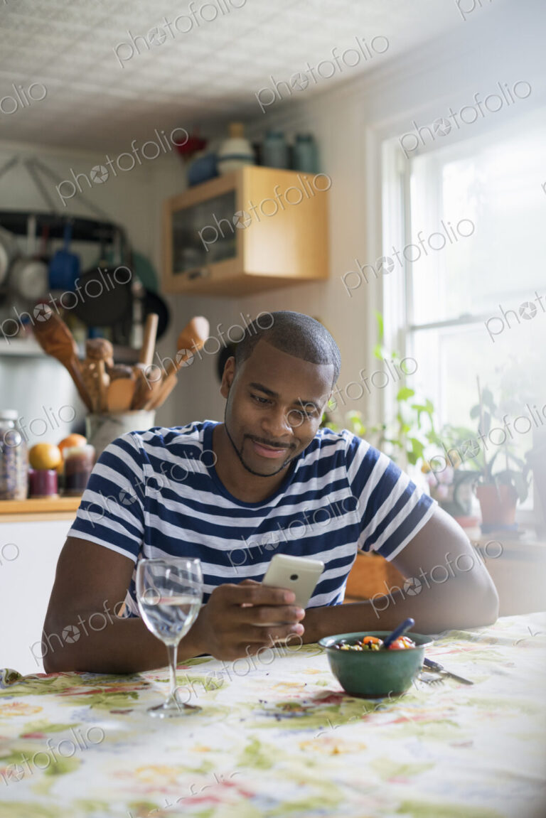 A man sitting at a table using a smart phone. Fruit dessert and a glass of wine at hand.