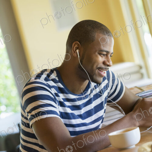 A man sitting in a cafe, having a cup of coffee, listening to music with headphones.