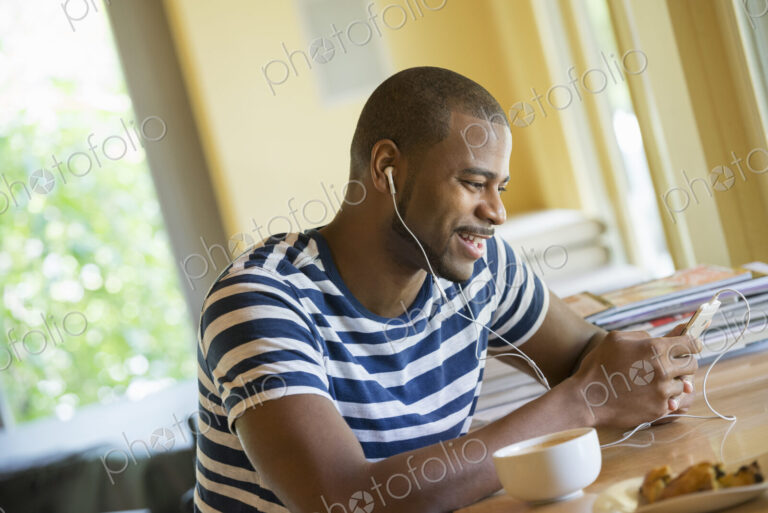A man sitting in a cafe, having a cup of coffee, listening to music with headphones.