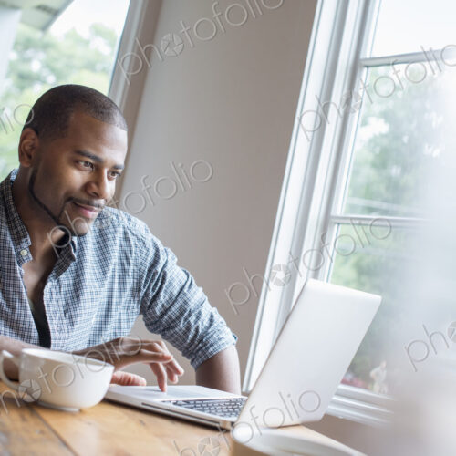 A man sitting in a cafe with a cup of coffee, using a laptop computer.