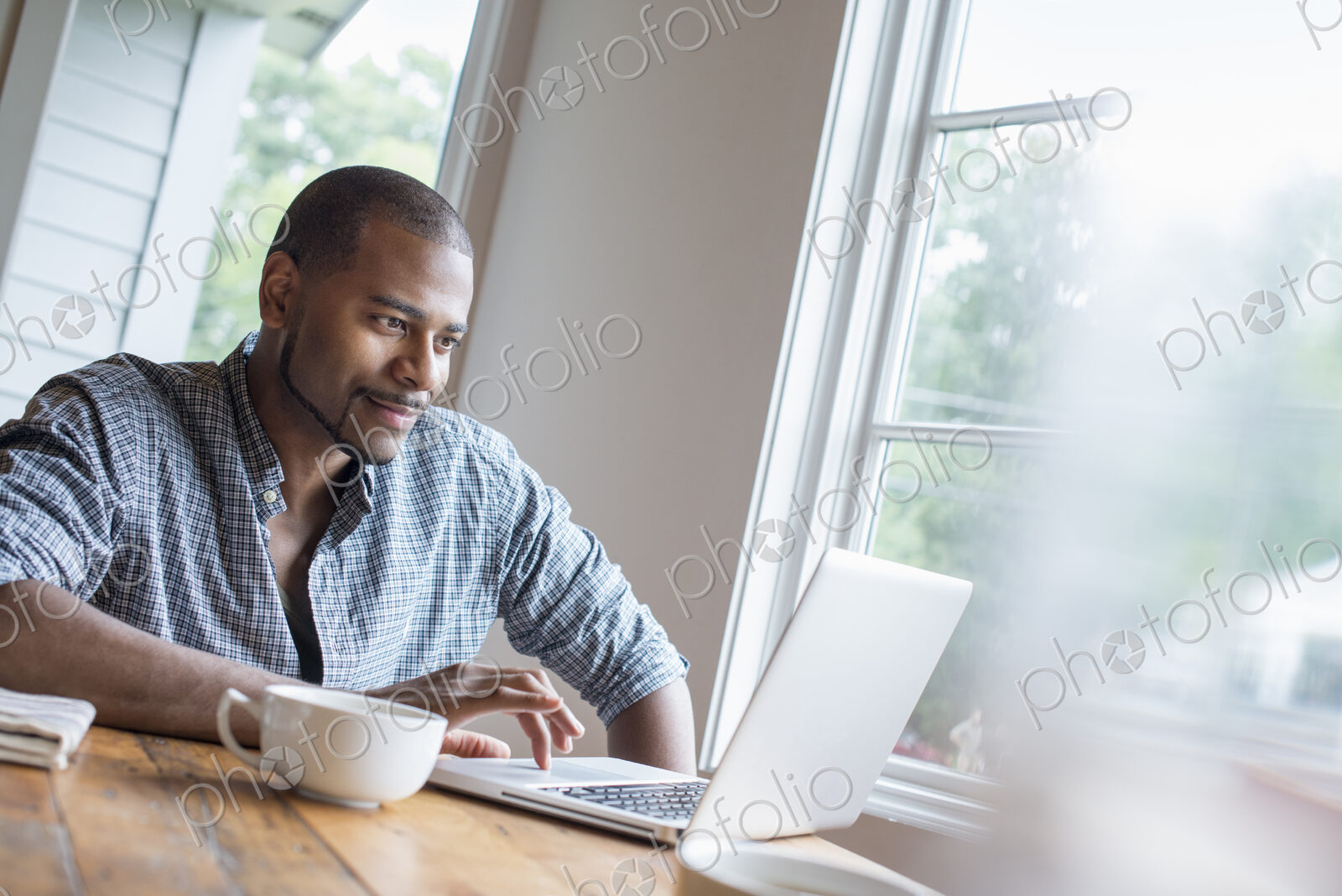 A man sitting in a cafe with a cup of coffee, using a laptop computer.