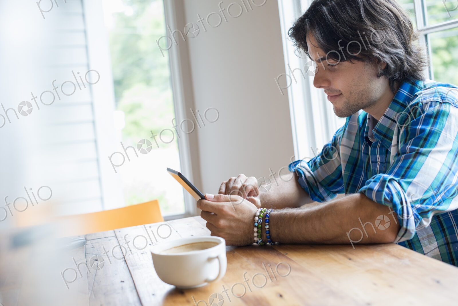 A man sitting in a cafe with a cup of coffee. Using a digital tablet.