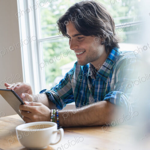A man sitting in a cafe with a cup of coffee. Using a digital tablet. A man sitting in a cafe with a cup of coffee. Using a digital tablet.