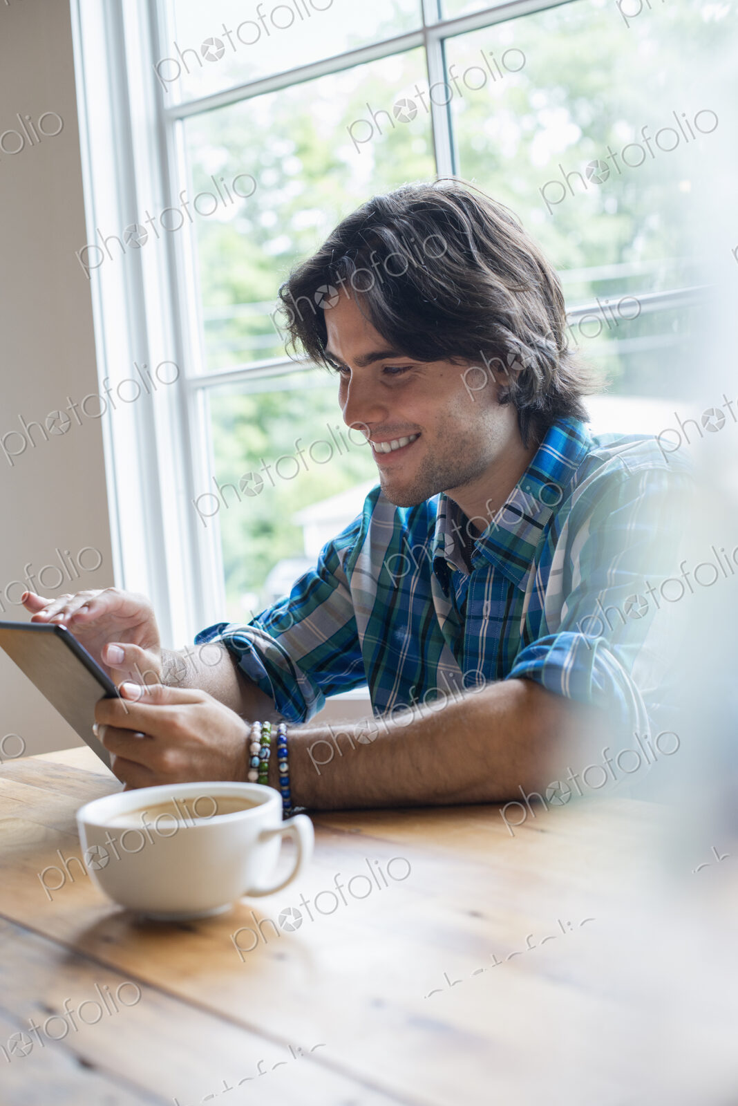 A man sitting in a cafe with a cup of coffee. Using a digital tablet.