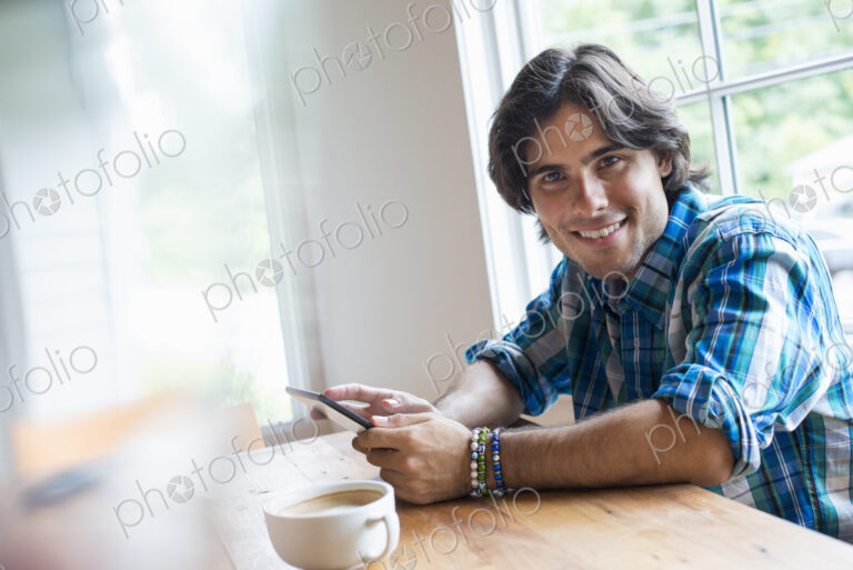 A man sitting in a cafe with a cup of coffee. Using a digital tablet.