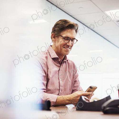 A man sitting in a classroom at a table and looking down at a cellphone. A man sitting in a classroom at a table and looking down at a cellphone.