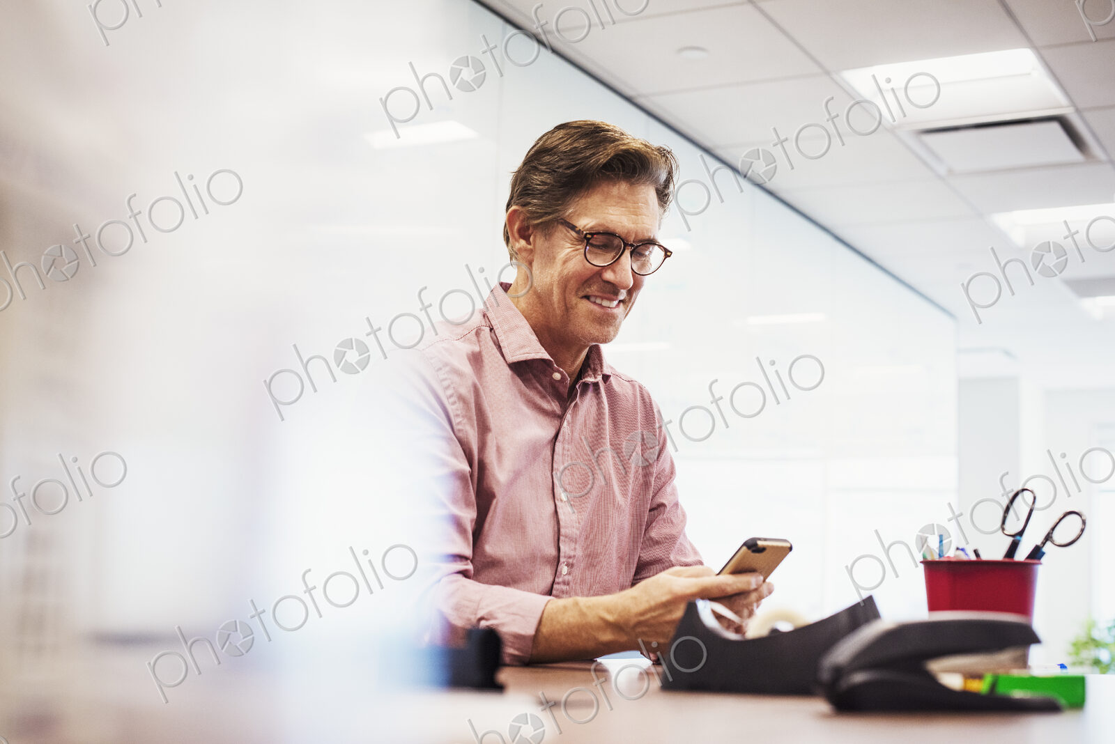 A man sitting in a classroom at a table and looking down at a cellphone.