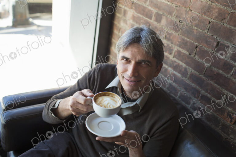 A man sitting in a coffee shop. Holding a cup of frothy cappuccino coffee.