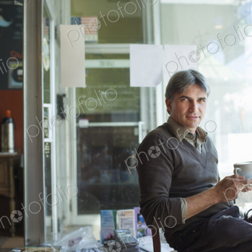A man sitting in a coffee shop. Holding a cup of frothy capucchino coffee.