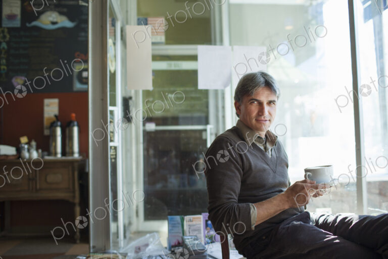 A man sitting in a coffee shop. Holding a cup of frothy capucchino coffee.
