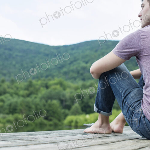 A man sitting on a wooden pier by a lake in summer A man sitting on a wooden pier by a lake in summer