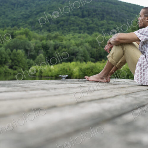 A man sitting on a wooden pier by a lake in summer A man sitting on a wooden pier by a lake in summer