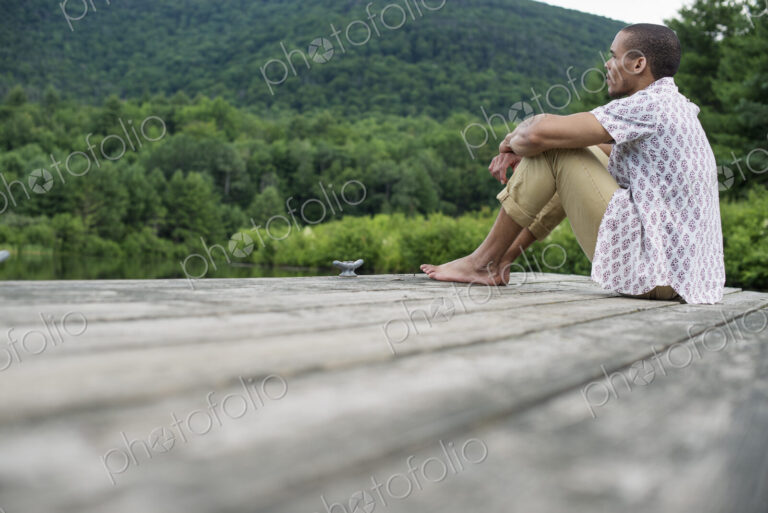 A man sitting on a wooden pier by a lake in summer