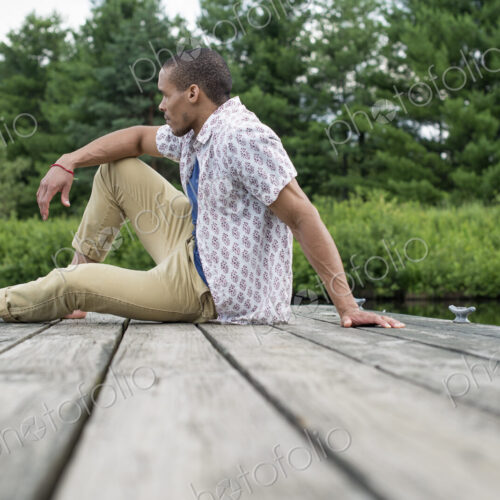 A man sitting on a wooden pier by a lake in summer A man sitting on a wooden pier by a lake in summer