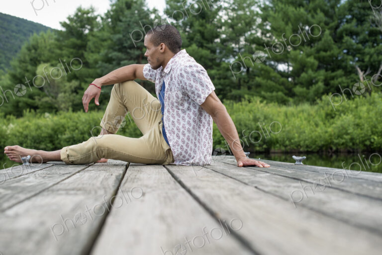 A man sitting on a wooden pier by a lake in summer