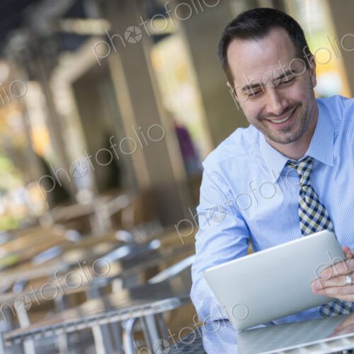A man sitting outdoors at a cafe table using a digital tablet. A man sitting outdoors at a cafe table using a digital tablet.
