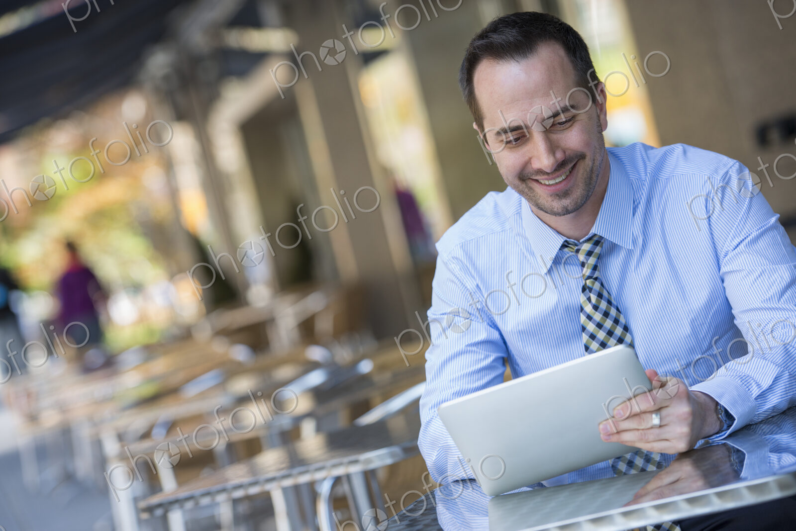 A man sitting outdoors at a cafe table using a digital tablet.